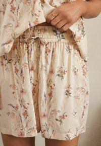 Ensemble de loungewear floral avec un fond crème et des motifs roses, violets et verts. Les shorts sont dotés d'une taille élastique avec un lien.