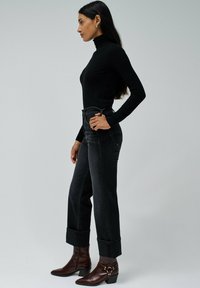 Črn pulover s turtleneck ovratnikom pod visokim pasom, temnimi jeansi s passenimi robovi. Rjave škornje z visokim peto in okrasno strojno opremo.