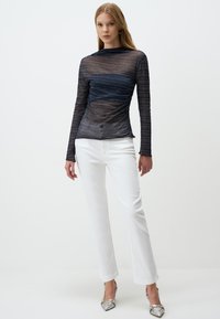 Top blu navy a maniche lunghe con righe orizzontali, materiale leggero e trasparente, e dettagli arricciati in vita, abbinato a jeans bianchi a gamba dritta.