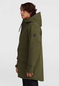 Olive zelená parka s kapucňou, ktorá má zips a gombíkový uzáver, predné vrecká a ribované manžety. Hladká, vodeodolná tkanina.