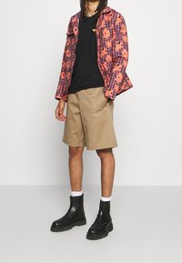 Multicolored plaid jacket in orange and purple, black T-shirt, beige shorts, and black zip-up boots with white socks. Simple design elements.