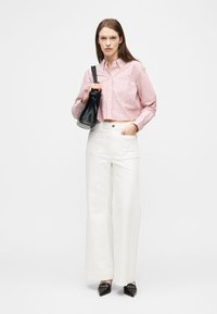 Γυναίκα που φοράει ριγέ κόκκινο και λευκό κοντό μπλουζάκι, λευκό παντελόνι με φαρδιά μπατζάκια, μαύρα μυτερά παπούτσια και κρατάει μαύρη τσάντα στον ώμο της.