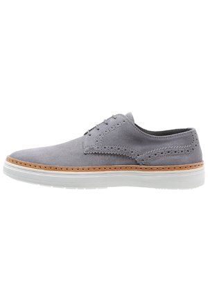 Chaussure décontractée en daim gris clair à lacets avec des détails brogue à bout golf, bordure beige et semelle extérieure en caoutchouc texturé blanc, vue latérale.