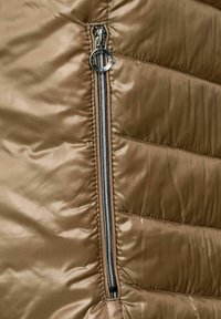 Brun vadderad jacka med en jämn, glänsande textur. Har en metallisk dragkedja med en rund dragremsa på vänster sida.
