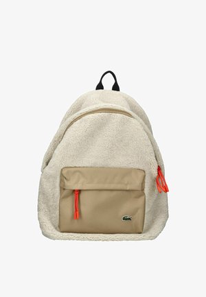 Beige batoh s fleecovým povrchem, dvěma zipovými kapsami, oranžovými šňůrami a malou zelenou nášivkou na přední kapse.