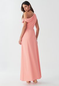 Gara, plecu daļu atsegta korāla krāsas kleita ar drapētu izgriezumu, gludu tekstūru un piegulošu vidukļa daļu. Kleita līdz grīdai ar smalkiem savārījumiem uz piedurknēm.