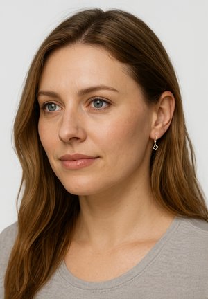 Goldohrringe in abstrakter Form, mit einem zarten Design und glatter Oberfläche, getragen von einer Person mit langen, welligen Haaren.