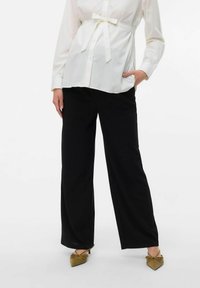 Chemise blanche à boutons avec une ceinture en cravate, associée à un pantalon large noir et des chaussures à bout pointu vert olive. Tissu lisse, coupe décontractée.