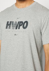 Camiseta de algodón gris con cuello redondo, que presenta en la parte delantera grandes letras negras "HWPO" y "HARD WORK PAYS OFF".