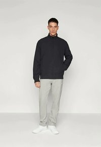 Svart zip-up jacka med hög krage, tillsammans med ljusgrå sweatpants och vita skor. Enkelt design med en avslappnad passform.