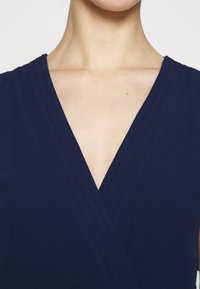 Robe portefeuille bleu marine avec un col plissé en forme de V profond. Texture de tissu lisse avec un léger éclat. Aucune décoration visible.