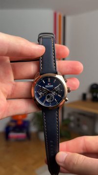 Jūras spēku ādas siksniņas pulkstenis ar rozā zelta tonī apvalku, zilu ciparnīcu, baltām atzīmēm un trim melniem apakšciparnīcām; atšķirīgs izšuvums.