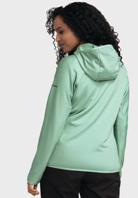 Mintgrüne Kapuzenjacke mit gerippter Textur, Akzentnähten und taillierter Silhouette, kombiniert mit schwarzen Hosen.