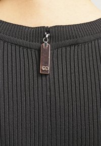 Černá, žebrovaná tkanina s vertikálními pruhy. Obsahuje zadní zip s obdélníkovým táhlem zvýrazněným logem. Hladká textura.