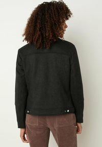 Giacca in suede nera con taglio dritto, dotata di yoke posteriore, regolazioni a scatto sull'orlo e dettagli di cucitura puliti e minimi.