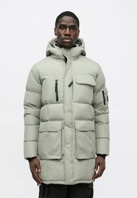 Ανοιχτό γκρι τζάκετ πούφ που διαθέτει κουκούλα, με τέσσερις μπροστινές τσέπες, μαύρους φερμουάρ και επικαλυμμ�ένη υφή για μόνωση.