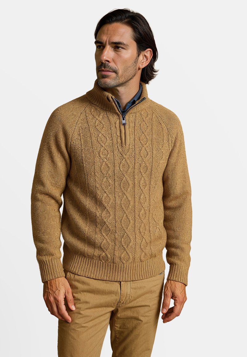 Pull en tricot beige avec un col montant et une fermeture éclair ; présente un motif en maille torsadée ainsi que des bords côtelés aux poignets et à l'ourlet. Porté avec une chemise à col.