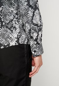 Long-sleeve shirt with a black and white snake print pattern, featuring a buttoned cuff and a straight hem, paired with black fabric.