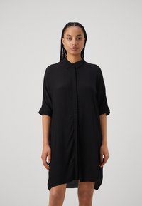 Schwarzes Button-up-Kleid mit aufgerollten Ärmeln, aus leichtem Stoff, mit geradem Schnitt und dezenten Falten vorne. Kürzerer Saum hinten.