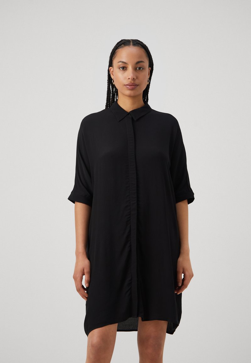 Schwarzes Button-up-Kleid mit aufgerollten Ärmeln, aus leichtem Stoff, mit geradem Schnitt und dezenten Falten vorne. Kürzerer Saum hinten.