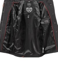 Interior de una chaqueta de lana negra con un forro de satén suave, acentos rojos y una etiqueta. Presenta múltiples bolsillos y cierres de botones.