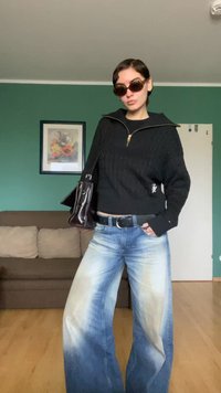 Musta, kaapelineuleesta valmistettu lyhyt villapaita vetoketjullisella kauluksella, siniset leveälahkeiset farkut haalistuneella pesulla ja tumma käsilaukku. Ruskeat ylisuuret aurinkolasit.