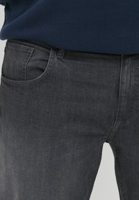 Dark gray denim jeans with a smooth texture, featuring a front pocket and subtle stitching details, paired with a navy sweater.