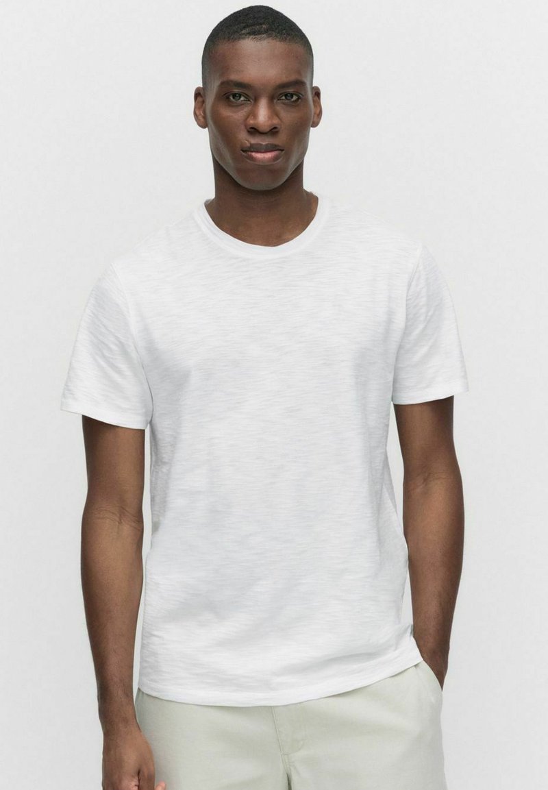 Hvid kortærmet t-shirt med en glat tekstur og rund halsudskæring. Tøjet har et diskret meleret mønster.