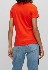 Pomarańczowy t-shirt z krótkim rękawem wykonany z bawełny, z okrągłym dekoltem i luźnym krojem, zestawiony z jasnoniebieskimi dżinsami z kieszeniami.