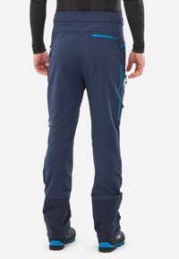 Les pantalons softshell navy présentent une coupe slim, une taille élastiquée, des poches zippées et des accents bleus contrastants sur les coutures et les zippers.
