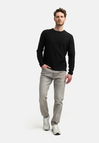Black long-sleeve shirt paired with light gray jeans and white sneakers. The shirt features a textured fabric and crew neckline.