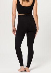 Leggings neri a vita alta in tessuto elastico, con una texture liscia e un design aderente, abbinate a un crop top coordinato.