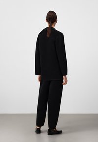 Haut noir à manches longues côtelé associé à un pantalon ample assorti. Tissu texturé, coupe décontractée et léger éclat sur les chaussures.