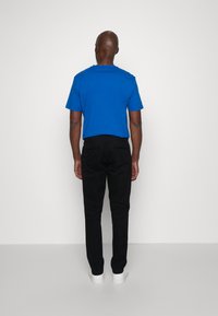 T-shirt in cotone blu, pantaloni neri e sneaker bianche. La T-shirt ha un collo a giro e i pantaloni presentano un taglio dritto con tasche posteriori.