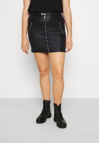 Mini falda negra de cuero sint�ético con cremallera frontal, dos bolsillos con cremallera y una cinturilla alta. Combinada con botas de combate negras de cordones.
