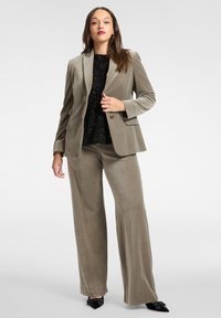 Completo in velluto color taupe composto da giacca aderente con rever a incavo e pantaloni a gamba larga. Top nero con paillettes sotto, scarpe nere appuntite.