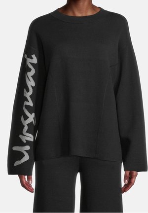 Sort langærmet sweater med oversized pasform, med store lysegrå skriftbogstaver på højre ærme.
