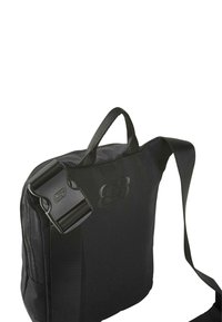 Bolsa de mensajero negra hecha de un tejido resistente, con una correa desmontable, un asa en la parte superior y un acento de logo texturizado en el frente.