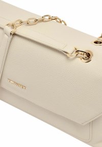 Borsa beige con texture, decorata con dettagli in catena dorata, dotata di chiusura a patta e logo impresso, che mette in risalto un design elegante e moderno.