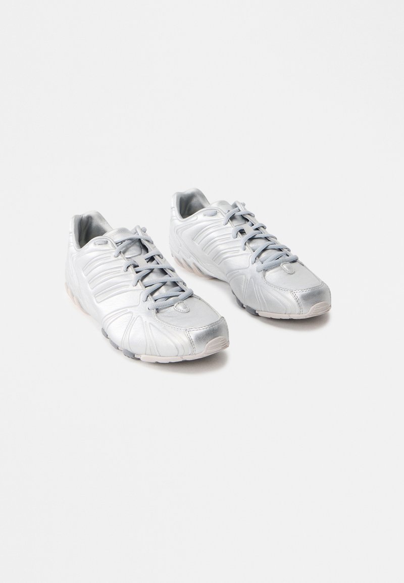 Αθλητικά παπούτσια σε ασημί απόχρωση με λεία και γυαλιστερή υφή; καμπυλωτός σχεδιασμός; γκρίζα κορδόνια; καουτσούκ σόλες με μοτίβα πρόσφυσης; στρογγυλή μύτη.