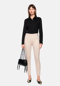 Black long-sleeve polo shirt with a collar; light beige fitted pants; black handbag with short handles; black flats with gold accents.