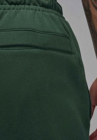 Pantaloni da jogging verde scuro realizzati in tessuto morbido, caratterizzati da una cintura con coulisse e una tasca posteriore con dettaglio di cucitura orizzontale.