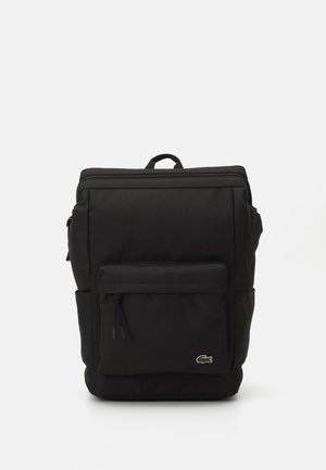Black rectangular backpack with top handle, front zip pocket, side pockets, and small green crocodile logo on lower right corner.