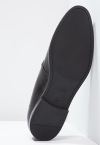 Semelle de chaussure en cuir noir avec surface texturée et bords lisses. Présente un logo discret et un bout arrondi. Design adapté pour une tenue formelle.