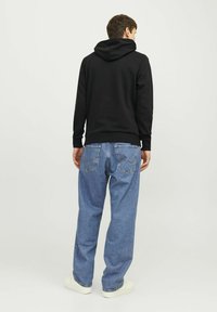 Sudadera negra con capucha y puños acanalados, combinada con unos vaqueros sueltos de tiro claro que tienen bolsillos traseros y detalles de costura. Zapatillas blancas.