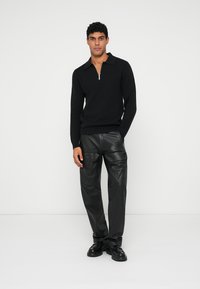 Sweater preto com fecho e colarinho, combinado com calças cargo de couro pretas. Textura suave, design ajustado e detalhes subtis.