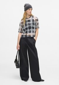 Top a righe trasparente in nero, bianco e beige con un design corto. Abbinato a pantaloni neri a vita alta e ampi, e un berretto grigio lavorato a maglia.