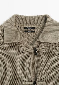 Cardigan gris en maille 100 % coton, avec col à revers, fermeture à boutons à bascule à l'avant et motif texturé en maille ajourée.