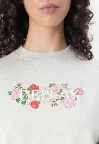 Grijze sweatshirt met een geborduurd bloemenontwerp van roze en rode rozen, verfraaid met gouden letters die "REPLAY" spellen. Gelaagd stof.