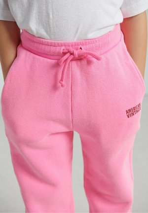 Pink sweatpants made of soft fabric, featuring an elastic waistband with drawstring and side pockets. "American Vintage" logo in brown.